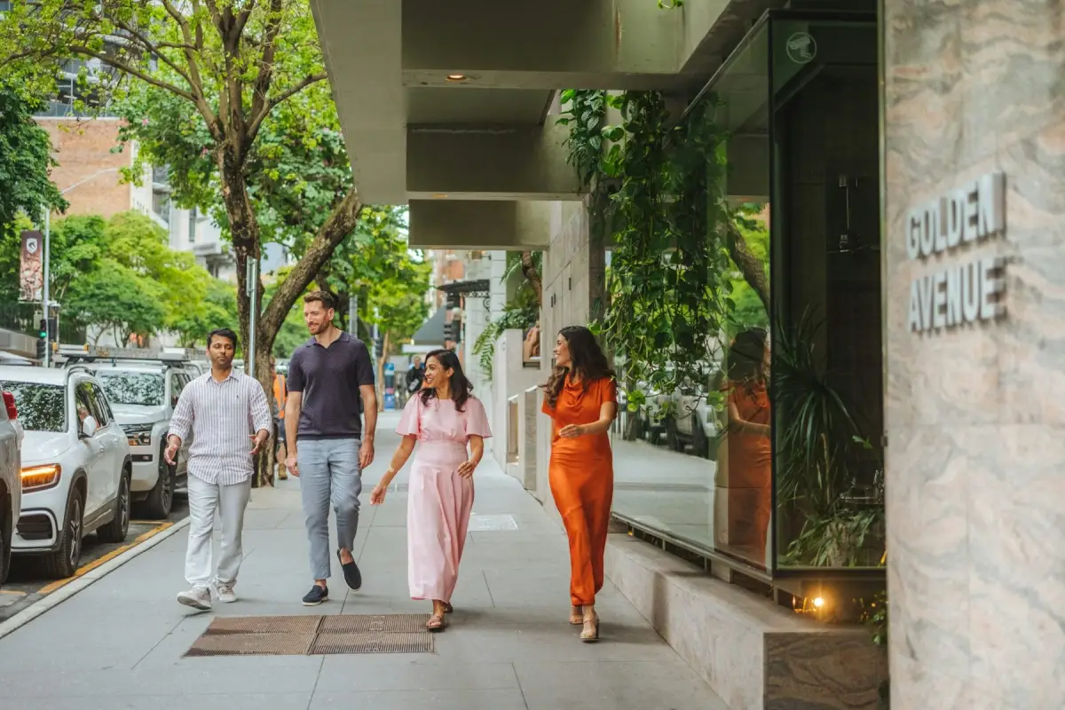 Four people walking and talking along a leafy Brisbane city street